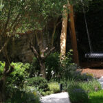 Curving garden path through lavender and shade planting beneath an olive tree with a hanging swing
